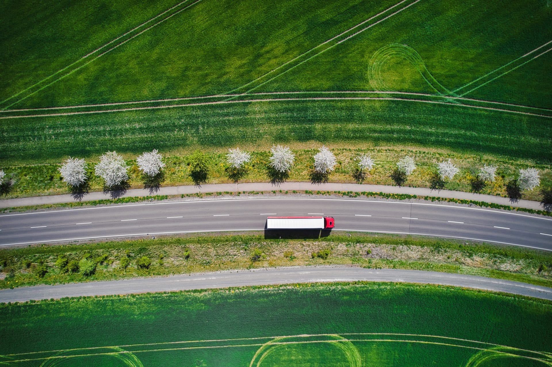 Aerial view of a road cutting through vibrant green agricultural fields.