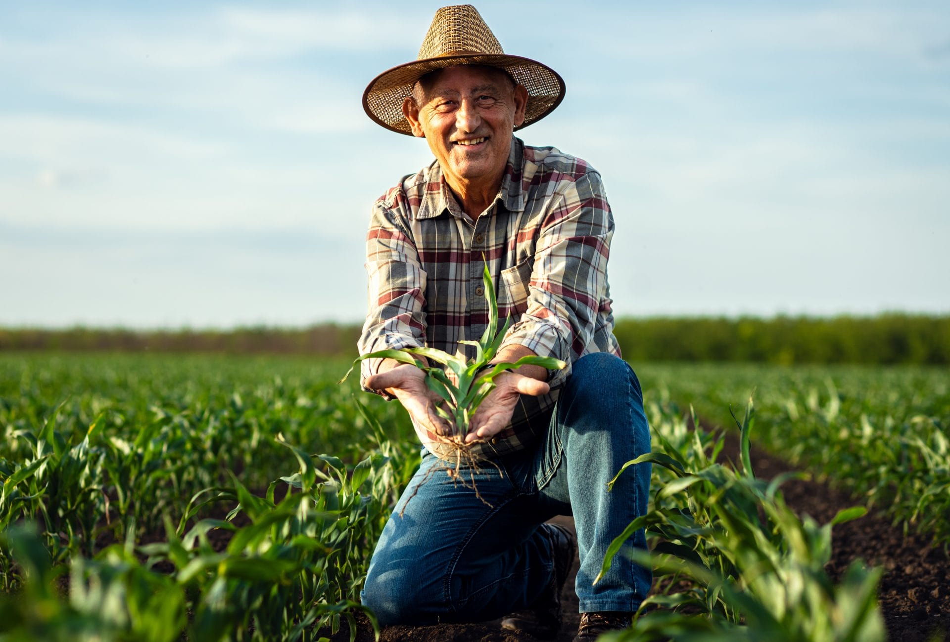 Farmer sitting in a field at sunrise or sunset, wearing a hat and casual work clothes.